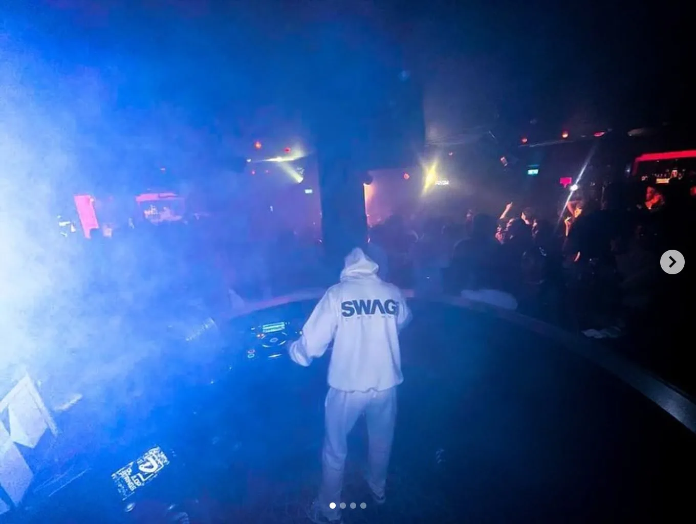 BDJ in a white hoodie behind the decks, blue smoke across the floor
