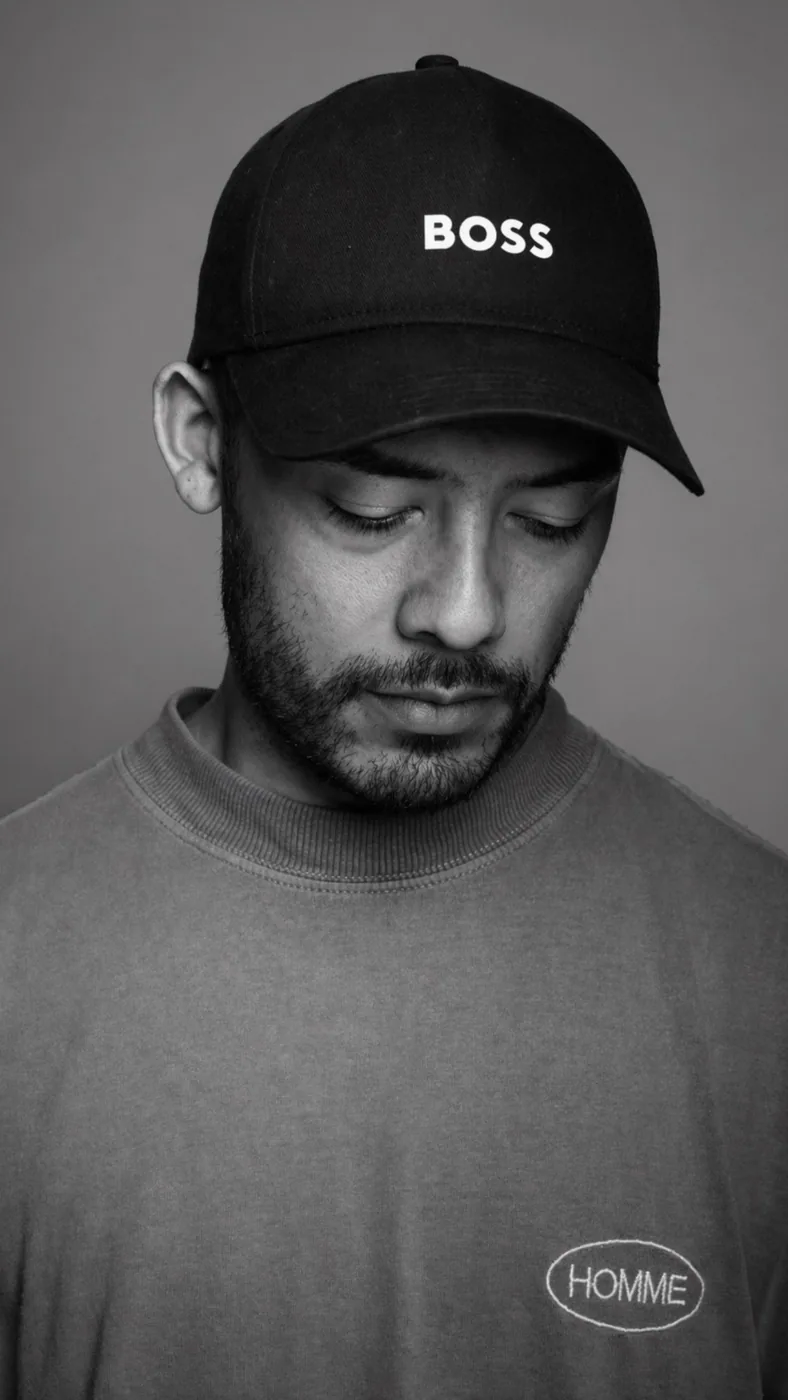 Black and white studio portrait of BDJ beneath a black cap